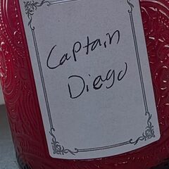 A red carved-glass candle jar with a handwritten label reading Captain Diego.
