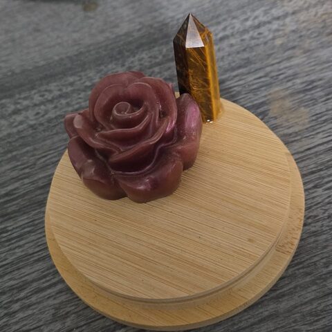 An incense altar piece: a deep red rose with an amber crystal point on a round bamboo base.